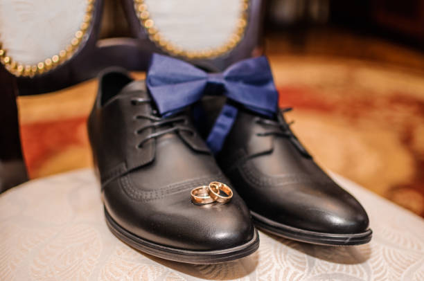 blaue fliege und goldene eheringe auf schwarzen kleid schuhe - shoe groom wood luxury stock-fotos und bilder
