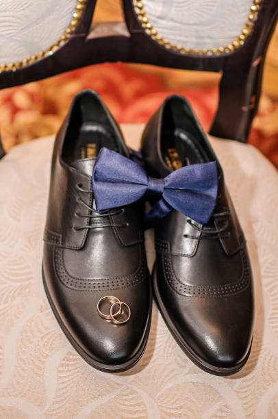gravata borboleta azul e anéis de casamento dourados em sapatos pretos - couple gold pair vertical - fotografias e filmes do acervo