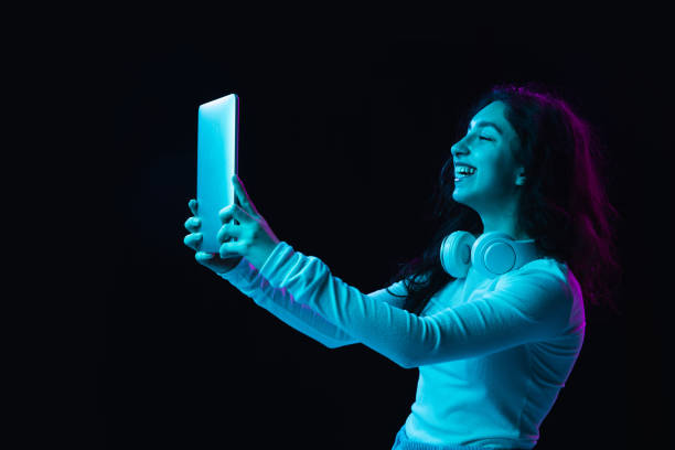 istock Young beautiful girl using device isolated on dark background in neon light 1308419212