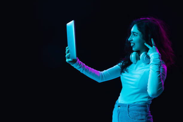 istock Young beautiful girl using device isolated on dark background in neon light 1308419219