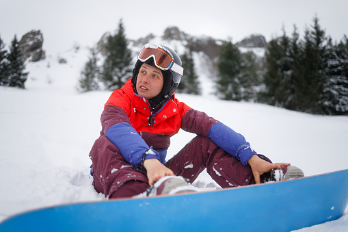 Photo of a young woman sitting on the snow and preparing for snowboarding on the ski slopes.