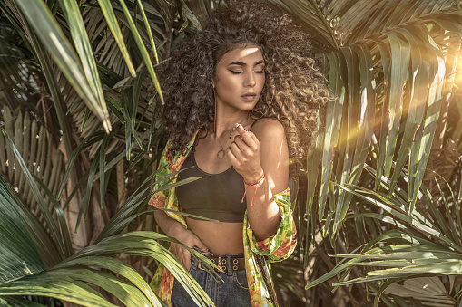 Portrait of natural beautiful afro woman posing over green palm's leafs.. Colombian young girl with curly hair.
