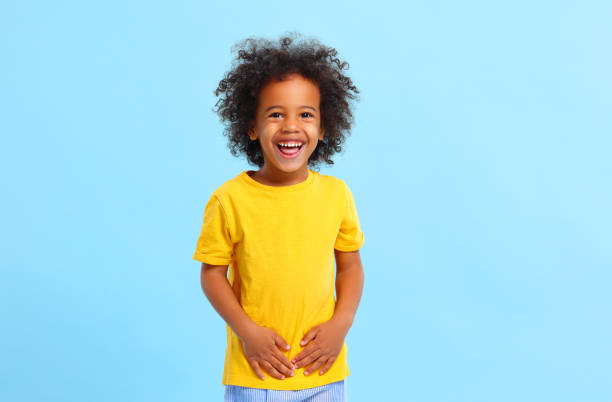 Positive African American little boy laughing in blue studio Delighted little black kid with Afro hair in casual clothes laughing and looking at camera against blue background preschool student stock pictures, royalty-free photos & images