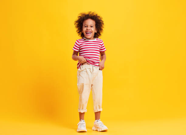 istock Cheerful ethnic cute kid standing and laughing  in yellow studio 1308421518
