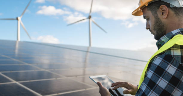 再生可能エネルギー農場でデジタルタブレットを扱う若者 - エコとテクノロジーのコンセプト - 耳に焦点を当てる - industrial windmill ストックフォトと画像