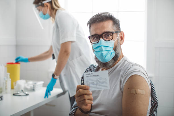 Mature men after coronavirus vaccination Mature man holding a card with details of his covid-19 vaccination. . Virus protection. COVID-2019. immunization certificate photos stock pictures, royalty-free photos & images