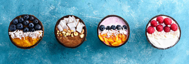 toppvy fyra färgglada smoothie skålar med blåbär, hallon, fysalis och kokosspån i kokosskålar på turkos bakgrund - yoghurt chocolate bowl bildbanksfoton och bilder