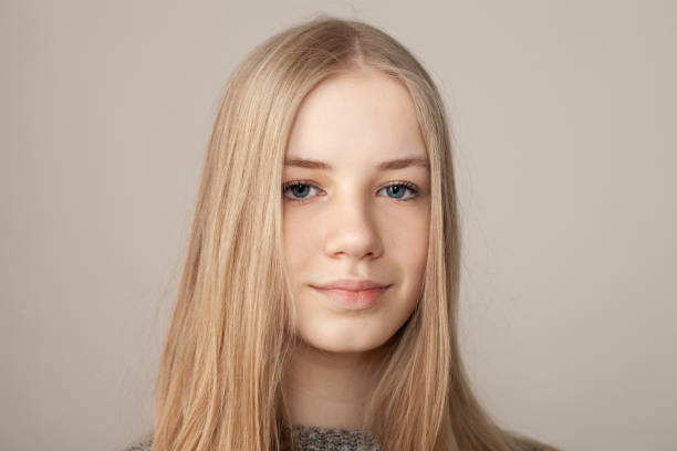 Studio portrait of blonde teenage girl Close up studio portrait of blonde teenage girl with long hair in gray sweater on beige background 15 year old blonde girl stock pictures, royalty-free photos & images