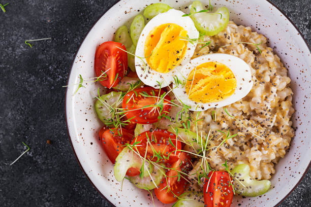 istock Breakfast oatmeal porridge with boiled egg, cherry tomatoes, celery and microgreens. Healthy balanced food. Top view, above, copy space 1308425049