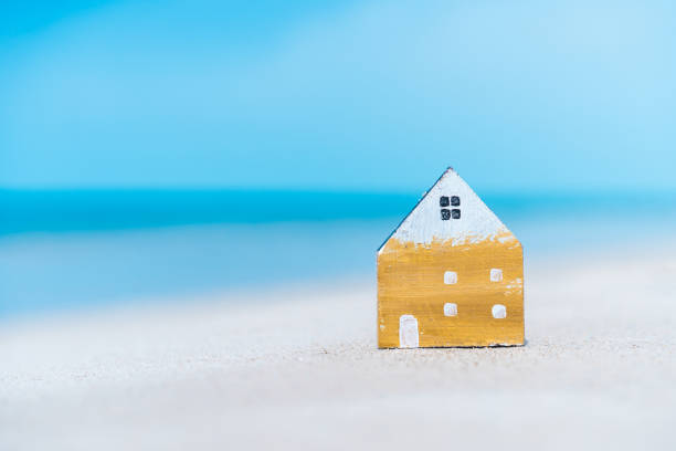 istock Small home model on sand beach with blue sky and white clouds background. 1308425120