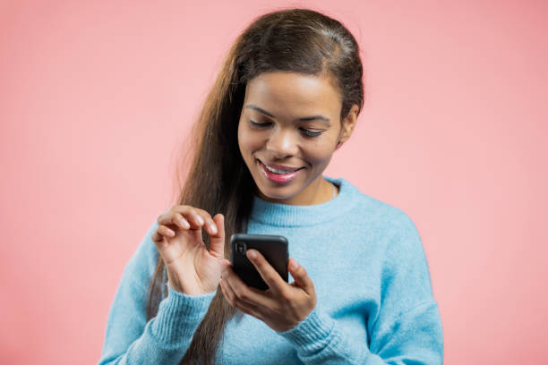istock African woman using smartphone on pink studio wall. Using modern technology - apps, social networks. 1308425192