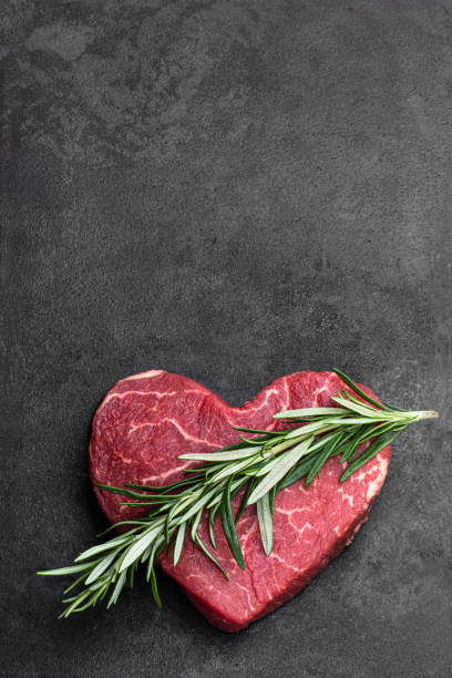 bistecca di manzo fresco crudo a forma di cuore con bastoncino di rosmarino su sfondo metallico - raw potato immagine foto e immagini stock