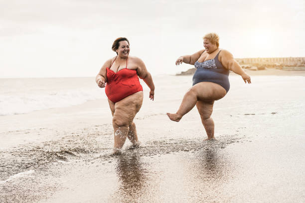 istock Plus size friends walking on the beach having fun during summer vacation - Focus on faces 1308425988
