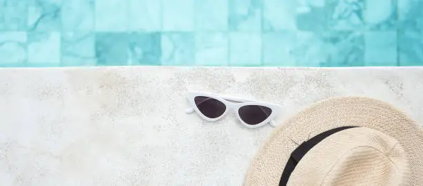 Photo of white sunglasses and hat near swimming pool in luxury hotel. Summer travel, vacation, holiday and weekend concept