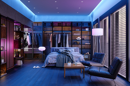 Habitación moderna interior por la noche con luz de neón. Cama desordenada, ropa en armario, sillones y lámpara de pie. photo