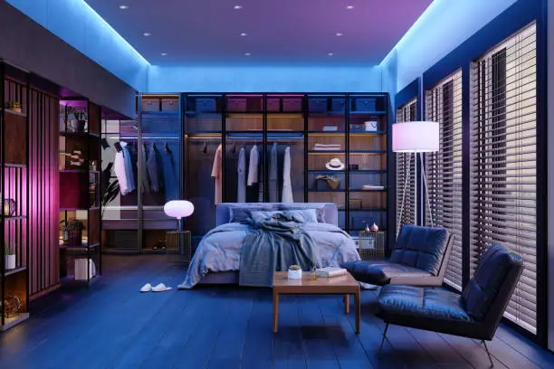 Photo of Modern Bedroom Interior At Night With Neon Light. Messy Bed, Clothes In Closet, Armchairs And Floor Lamp.