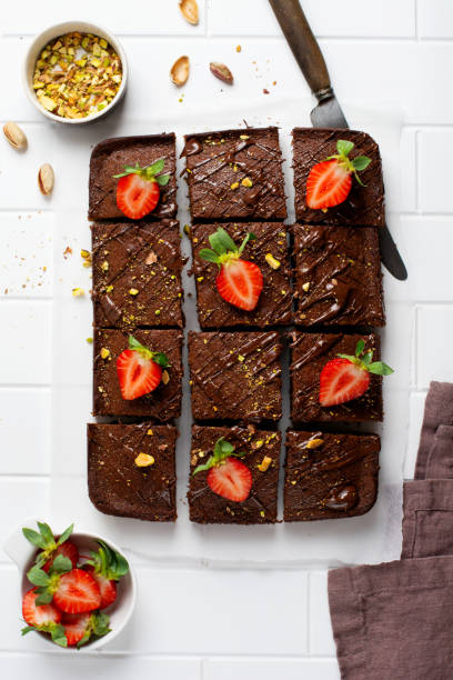 istock Chocolate squares with pistachio nuts and strawberries on white paper on a light background, top view, horizontal composition. Flat food 1308429495