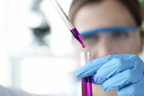 исследователь капает фиолетовую жидкость из пипетки в пробирку - reagent стоковые фото и изображения