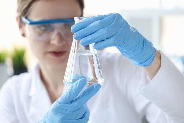 mujer científica sosteniendo frasco con líquido transparente en sus manos de cerca - experimento científico fotografías e imágenes de stock
