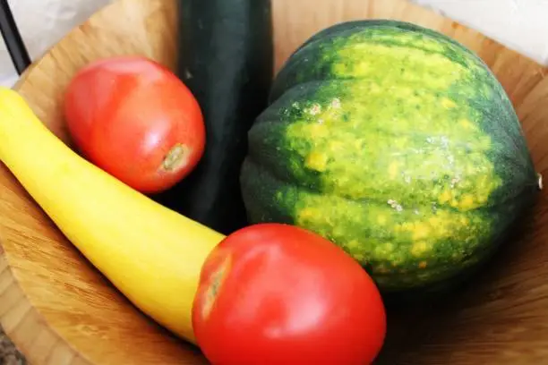 Assorted fresh vegetables in a wooden bowl.