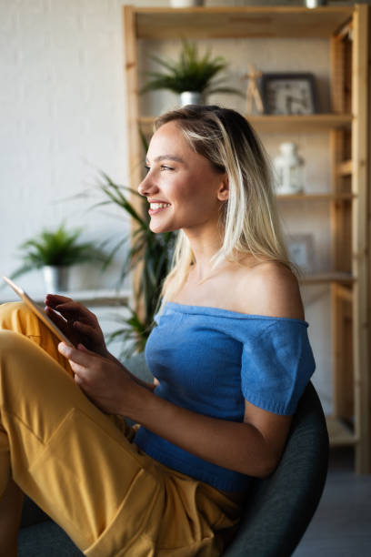 istock Relaxed young woman in sofa smiling content, happy and reading, working on tablet pc at home 1308431070