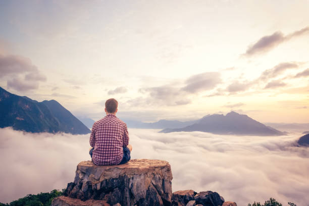 istock Man sitting on a summit with a beautiful view over the clouds 1308431296
