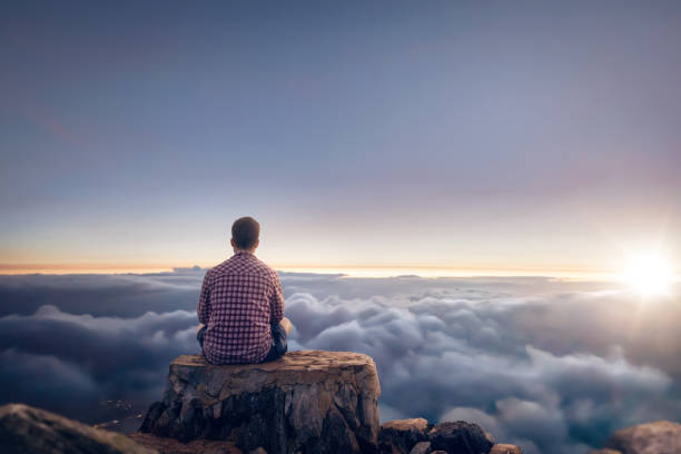 istock Man sitting on a summit above the clouds during sunrise 1308431312