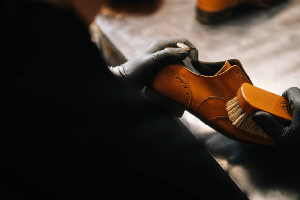 istock Close-up back view of unrecognizable shoemaker cleaning with brush old light brown leather shoes. 1308432345