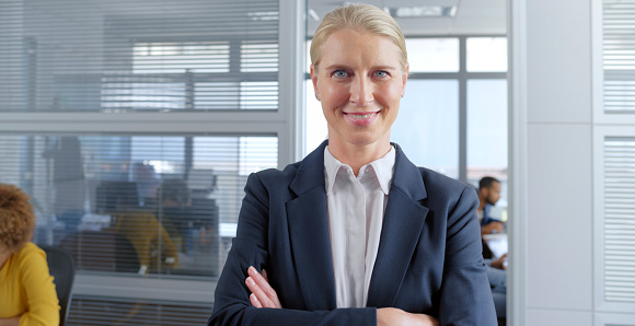Portrait of smiling mature businesswoman with arms crossed standing in office.