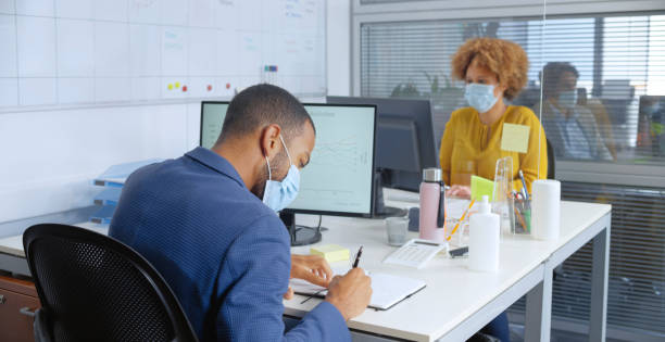 Business people working in office Businessman and businesswoman wearing protective face masks working in office during pandemic. office cubicle mask stock pictures, royalty-free photos & images