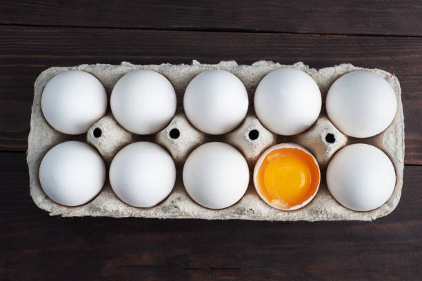 istock Fresh chicken eggs in a package, raw eggs in a white shell in a box. Top view copy space, wooden background. Broken egg with yolk. 1308433002