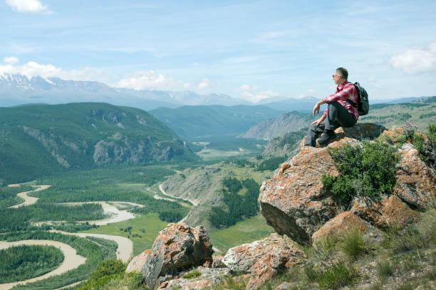istock Hiker man with backpack sitting on top of cliff and looking beautiful valley. 1308435446