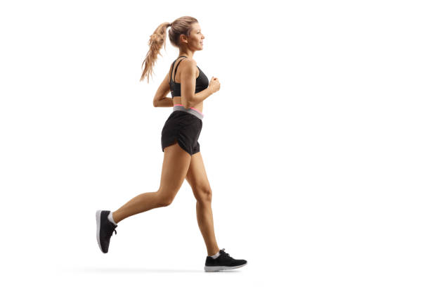 full length profile shot of a young female in black shorts and top running - running women jogging profile imagens e fotografias de stock