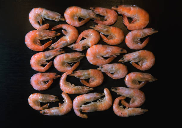 Tails of frozen shrimp and ice in pink bowl. Pink background. Close up. Top view. Copy space
