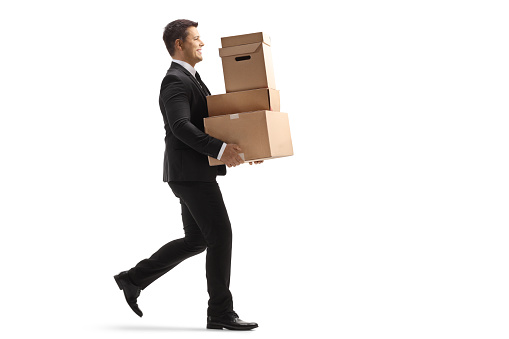 Full length profile shot of a businessman walking and carrying boxes isolated on white background