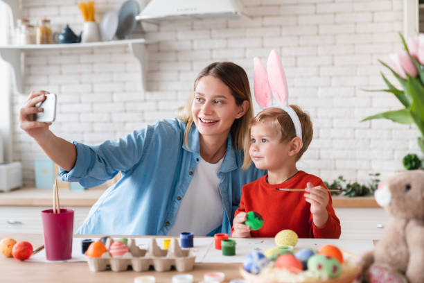 istock Happy mom and little son in bunny ears taking selfie while painting eggs for Easter 1308441823