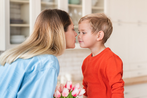 Young european mom kissing her little son for his tulips for celebration