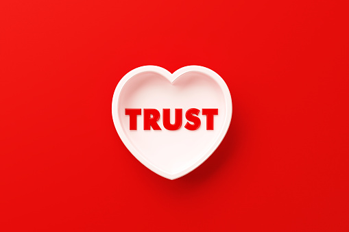 White heart shape with trust text sitting on red background.  Horizontal composition with copy space. Trust concept.