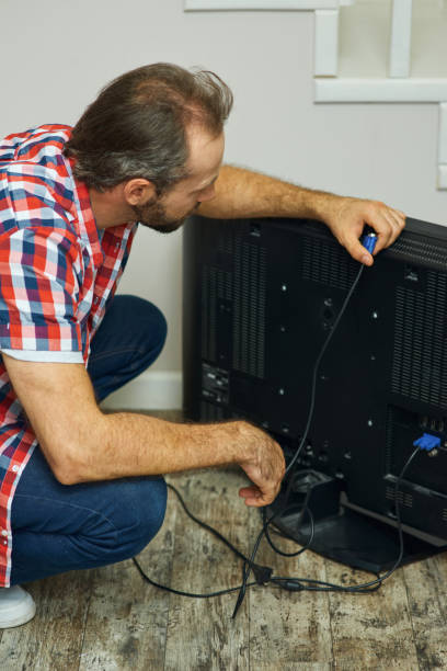 installation process. handyman looking focused, holding tv cable while installing or fixing tv set in apartment of a customer - men home interior screwdriver cable imagens e fotografias de stock