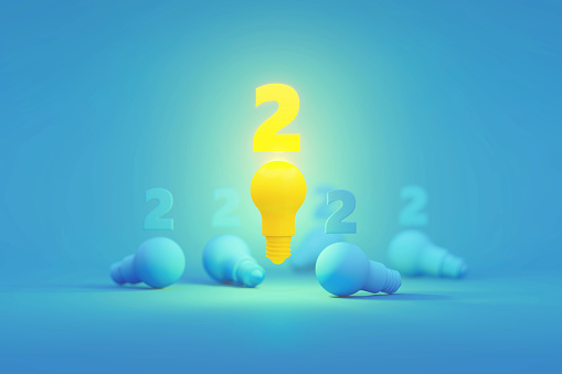 Yellow number 2 sitting above a glowing yellow light bulb surrounded by blue lightbulbs over blue background. Horizontal composition with copy space. Creativity and innovation concept.