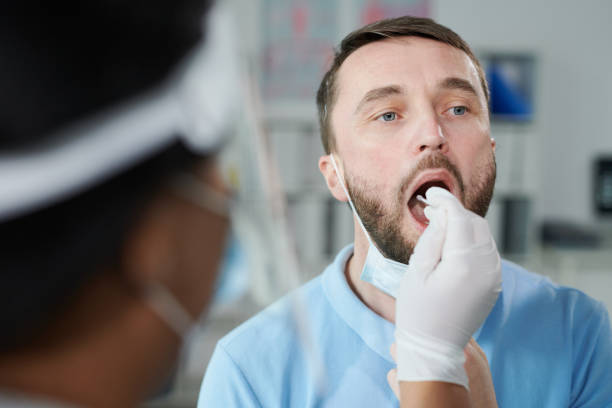 Face of young male patient being tested for covid with oral swab by gloved nurse Face of young male patient being tested for covid with oral swab held by gloved female nurse or clinician while sitting in front of her oral surgeon stock pictures, royalty-free photos & images