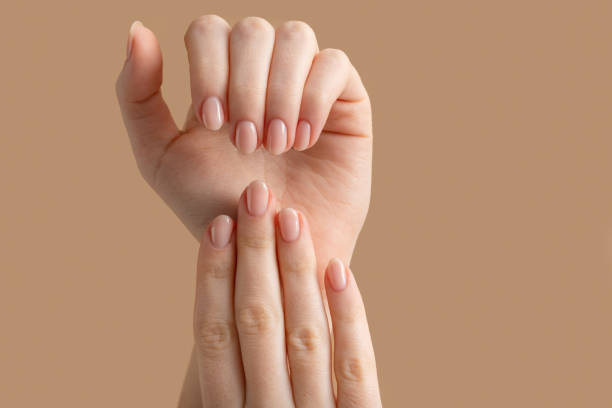 hände einer schönen gepflegten frau mit femininen nägeln auf beigefarbenem hintergrund. maniküre, pediküre schönheitssalon konzept. leerer platz für text oder logo. auf nägeln nackt gel politur - fingernagel stock-fotos und bilder