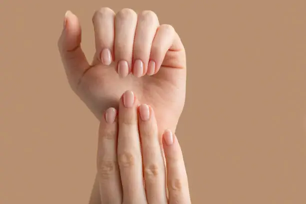 Photo of Hands of a beautiful well-groomed woman with feminine nails on a beige background. Manicure, pedicure beauty salon concept. Empty space for text or logo. On nails nude gel polish