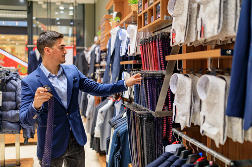 Closeup of smiling early 30's handsome man choosing some clothes at retail store in local shopping mall.