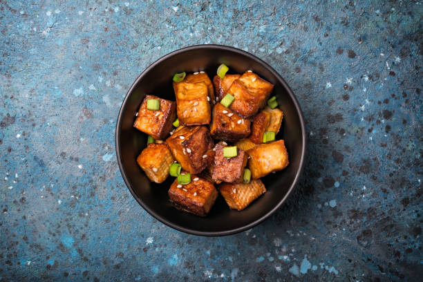 Fried tofu with sesame seeds and green onion Top view of fried tofu with sesame seeds and green onion for healthy vegan and vegetarion nutrition on blue concrete background tofu stock pictures, royalty-free photos & images