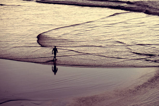 istock Man walks towards the ocean for a swim 1308453297