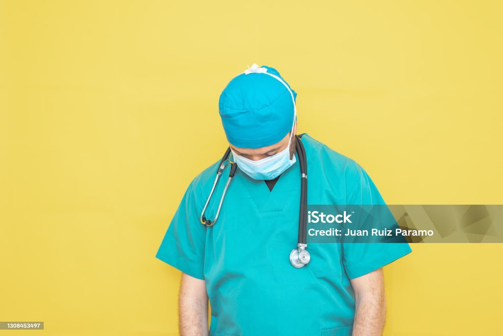 doctor dressed as a surgeon in green with stethoscope and mask on a yellow background with a worried expression. Adult Stock Photo