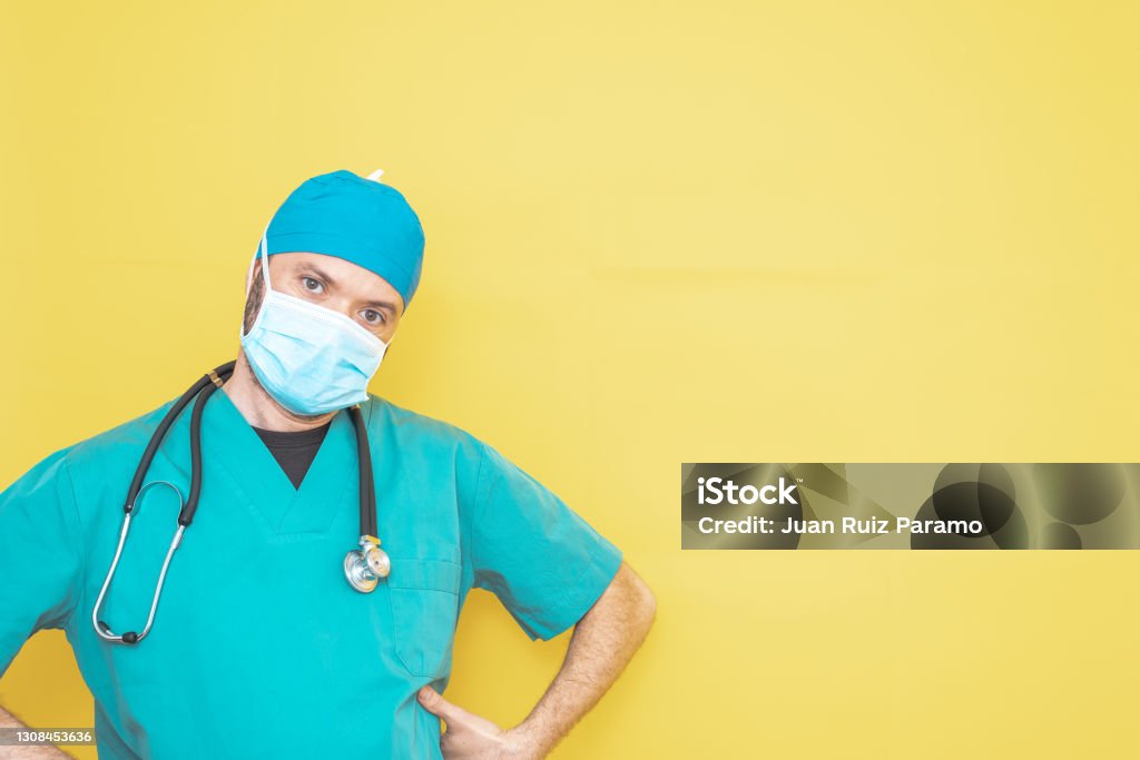 doctor dressed as a surgeon in green with stethoscope and mask on a yellow background with a worried expression. Adult Stock Photo