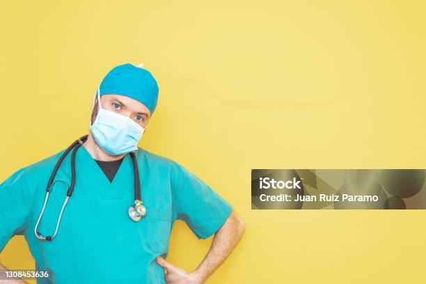 Doctor Dressed As A Surgeon In Green With Stethoscope And Mask On A Yellow Background With A Worried Expression Stock Photo - Download Image Now