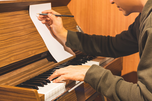 male composer playing piano and writing a song on music sheet